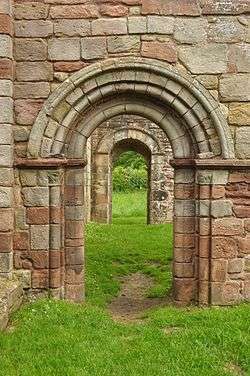 A photograph showing a round arch in a wall, with a similar arch beyond seen through it.