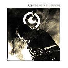 A record sleeve with a sepia-tone photograph of Bono holding a circular-shaped microphone in front of a thick fog. A white border surrounds the image and reads "U2 Wide Awake in Europe" at the top right.