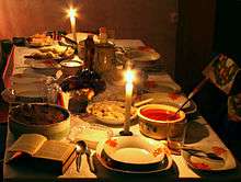 A table covered with a white cloth and set with an open Bible, candles and dishes of various foods