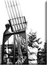 monochorome photograph of a man stood alongside of a device which comprises mainly a series of vertical pipes