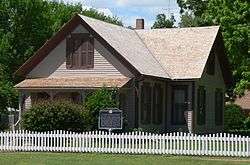 One-and-a-half-story house with gable roof and small front porch; surrounded by picket fence