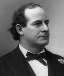 A man in his early forties, with receding black hair, facing right and wearing a black bow tie, black coat, and white shirt