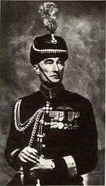 Formal portrait of man in dark-coloured dress uniform and headgear with braid and medals