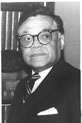 Black-and-white photo of an African American man in a suit wearing glasses looking to his left