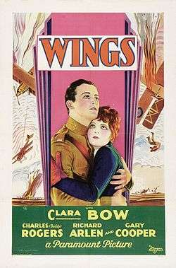 The theatrical poster of a movie. It focuses on two people. The man is wearing an aviator suit and the woman is wearing a blue jacket and red gloves.