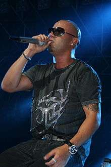 Wisin, seated, holding a microphone.