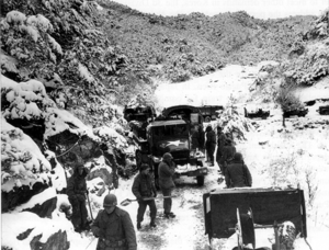 A group of soldier shoving snow in front of a convoy