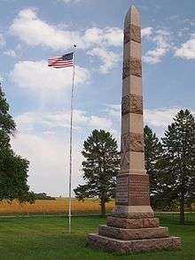 A tall stone spire to the right of a U.S. flag on a pole