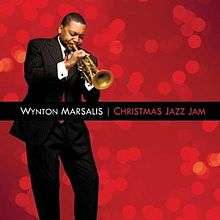 Before a red background, a man in a suit is playing a trumpet with his eyes closed; the text "Wynton Marsalis Christmas Jazz Jam" appears in a black bar across the center