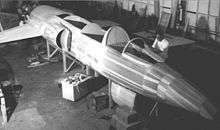 Black-and-white photograph of male personnel working on a wooden mock-up of jet aircraft