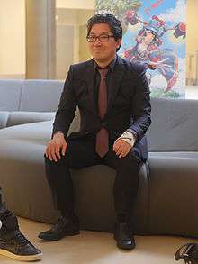 A photograph of the game's producer, Yuki Naka, in 2015. His left hand has a cast around it.