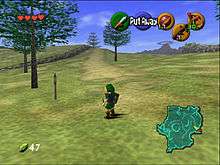 The child version of the game's protagonist, Link, stands in Hyrule field wearing his distinctive green tunic and pointed cap. In each corner of the screen are icons that display information to the player. In the upper left-hand corner there are hearts which represent Link's health, in the lower left-hand corner is a counter which displays the quantity of Rupees (the in-game currency) possessed by the player. There is a mini-map in the lower right-hand corner, and five icons in the upper right-hand corner, one green, one red, and three yellow, which represent the actions available to the player on the corresponding buttons of the N64 controller.