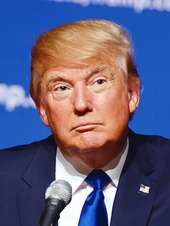 Headshot of presidential candidate Donald Trump, wearing a suit and behind a microphone