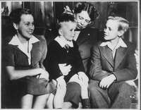 Three children sitting; a woman behind them